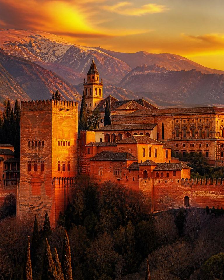 The Alhambra of Granada glowing at golden hour, with the Sierra Nevada behind.